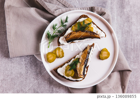 Close up of sandwiches with ricotta, pickles and sprats on rye bread on a plate on a table top view Close up of sandwiches with ricotta, pickles and sprats on rye bread on a plate on a table top view 136089855