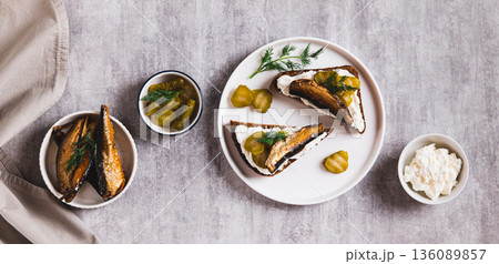 Rye bread toasts with cream cheese, sprats and pickles on a plate on the table top view web banner Rye bread toasts with cream cheese, sprats and pickles on a plate on the table top view web banner 136089857