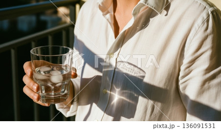 Person in White Shirt Holding a Cold Glass of Water with Ice 136091531