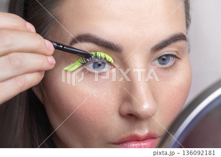 Caucasian woman twists her eyelashes on her own. A woman laminates eyelashes, applies cosmetics with a brush. close up photo Caucasian woman twists her eyelashes on her own. A woman laminates eyelashes, applies cosmetics with a brush. close up photo 136092181