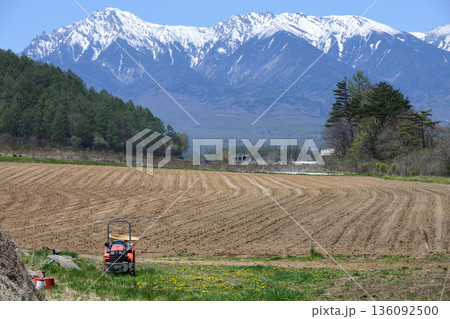 八ヶ岳を望む種まき前の畑の向こうからやって来る小海線ローカル列車 136092500