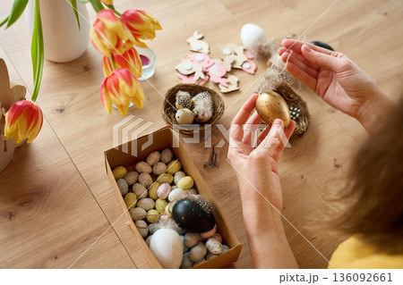 Woman decorating handmade Easter eggs with feathers at home 136092661