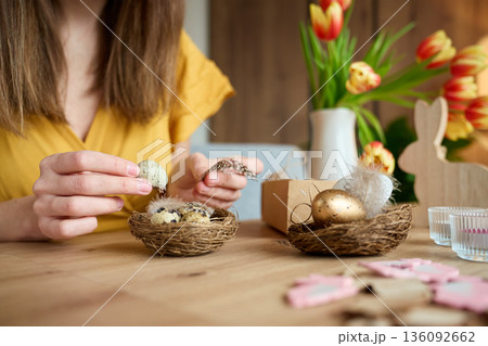 Woman decorating nest with speckled Easter eggs and feathers Woman decorating nest with speckled Easter eggs and feathers 136092662