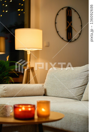 Living room interior with sofa, floor lamp, wall clock and lit candles 136092686
