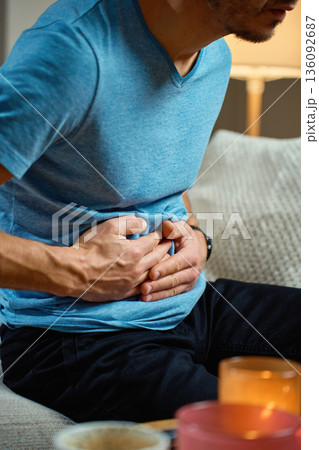 Man holding stomach while sitting on sofa at home Man holding stomach while sitting on sofa at home 136092687