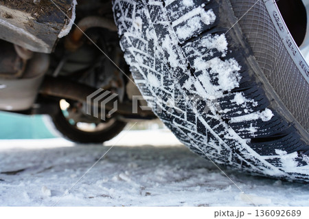 Winter car tire with snow on tread on icy road 136092689