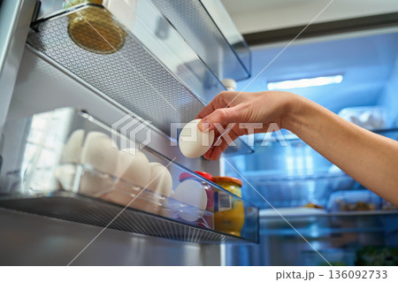 Hand taking egg from refrigerator door shelf 136092733