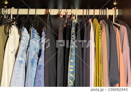Assortment of clothes hanging in a dark wardrobe Assortment of clothes hanging in a dark wardrobe 136092843