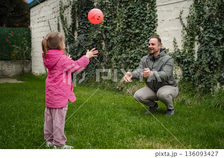 Father daughter playing catch with ball in backyard 136093427