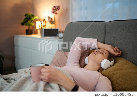 Woman lying bed suffering headache listening music Woman lying bed suffering headache listening music 136093453