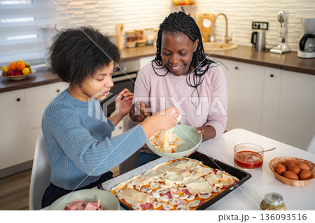 Mother and daughter preparing homemade pizza in kitchen 136093516