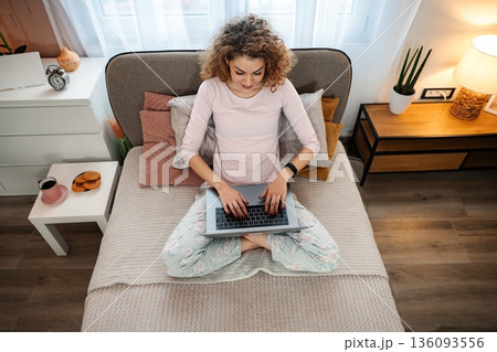 Young woman working remotely on laptop in bed 136093556