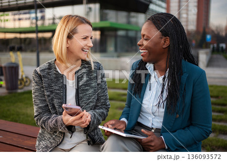 Diverse businesswomen laughing enjoying break with mobile technology Diverse businesswomen laughing enjoying break with mobile technology 136093572