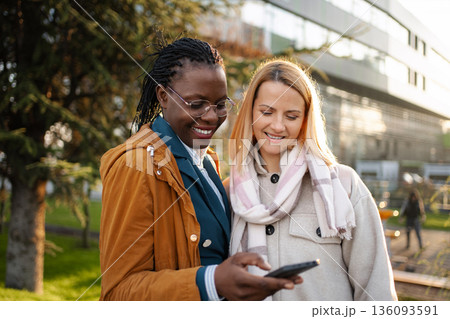 Diverse businesswomen using smartphone sharing content outdoors 136093591
