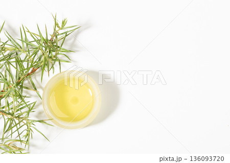 Top view to small round jar with essential juniper with fresh juniper leaves on white. Copy space 136093720