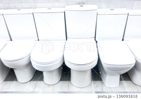 Assortment of ceramic toilet bowls are located in a plumbing store 136093818