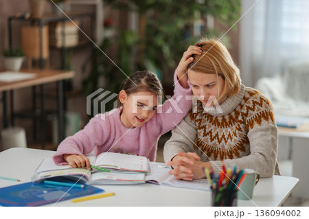 Young girl assisting her stressed mother with homework at home 136094002