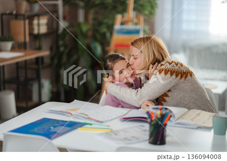 Mother kissing daughter while studying at home getting affection 136094008