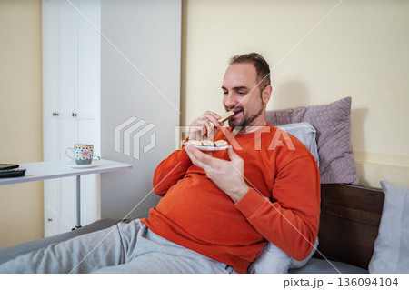 Adult man enjoying sweet cookies in bed at home 136094104