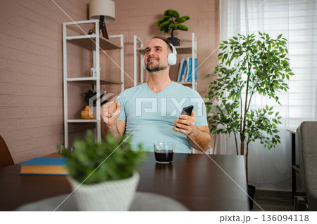 Man enjoying music on headphones at home, relaxing with coffee Man enjoying music on headphones at home, relaxing with coffee 136094118