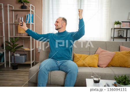 Happy man celebrating success watching smartphone video call Happy man celebrating success watching smartphone video call 136094131
