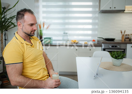 Mature adult man relaxing with healthy drink while looking at tablet 136094135