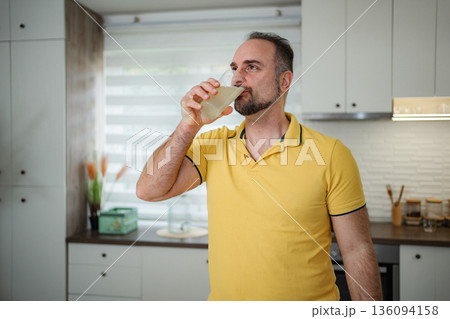Mature adult man drinking healthy beverage in kitchen Mature adult man drinking healthy beverage in kitchen 136094158