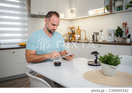 Man drinking coffee and using tablet in kitchen at home 136094162