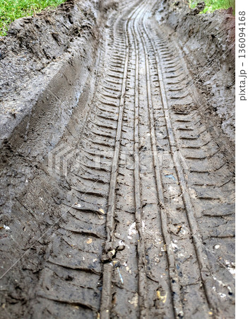Close Up of Muddy Thick Mud Tire Wheel Tracks on a Country Road Travelling Through Grass and Field. 136094168