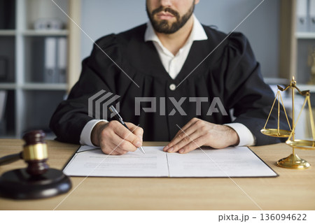 Judge signing legal documents at wooden desk with gavel, law and justice scales 136094622