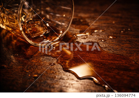 クローズアップ、木製デスクに倒れたウィスキーグラスから溢れ出る琥珀色のアルコール クローズアップ、木製デスクに倒れたウィスキーグラスから溢れ出る琥珀色のアルコール 136094774