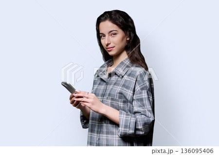 Smiling teenage girl holding smartphone on white studio background 136095406