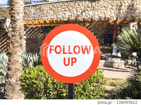 Follow up symbol. Concept word Follow up on beautiful red and white road sign. Beautiful palm tree and market background. Business follow up concept. Copy space. 136095622
