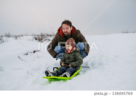 Dad and child bobbing downhill on snow slider. 136095769