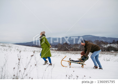 Winter family adventure with parents and little son sledding. 136095795
