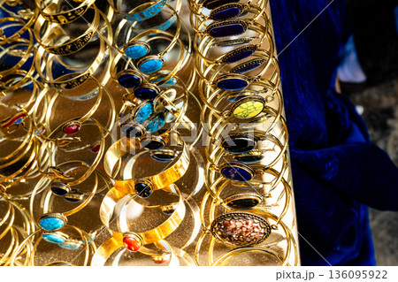 Golden jewelry displayed for sale at Khan El Khalili market in Cairo. Various bangles with colorful stones are arranged neatly on a table. 136095922