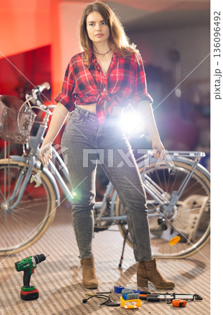 Woman holding wrenches repairing bicycle in workshop 136096492