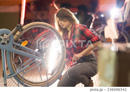 Woman repairing bicycle wheel in a bike workshop 136096542
