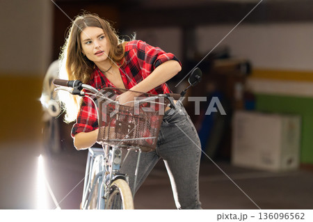 Young woman checking bicycle basket in parking garage Young woman checking bicycle basket in parking garage 136096562