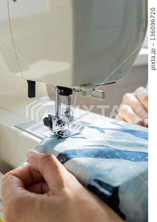 person sews product made blue fabric on sewing machine. tailor focused on work, calm relaxed mood.  136096720