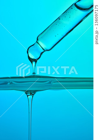 Serum dropper dispensing liquid on blue background 136097175