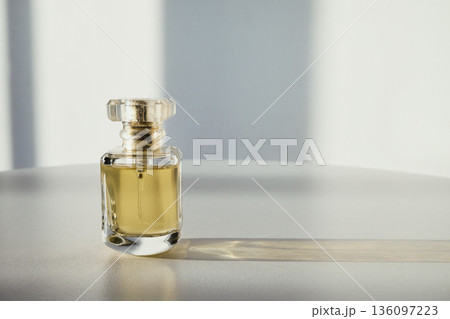 Perfume bottle with golden liquid reflecting natural light on clean surface Perfume bottle with golden liquid reflecting natural light on clean surface 136097223