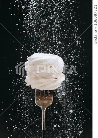 Powdered sugar falling over vanilla meringue on fork, black background Powdered sugar falling over vanilla meringue on fork, black background 136097521