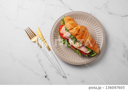Croissant sandwich with ham, mozarella cheese and arugula on a plate on a marble background Croissant sandwich with ham, mozarella cheese and arugula on a plate on a marble background 136097605