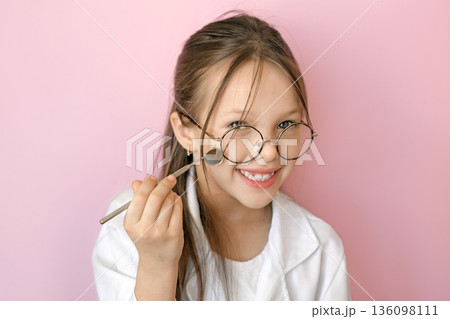 Smiling child dressed as dentist holding dental mirror on pink background. Concept of World Oral Health Day, oral hygiene awareness, healthy teeth, prevention and children dental healthcare. 136098111
