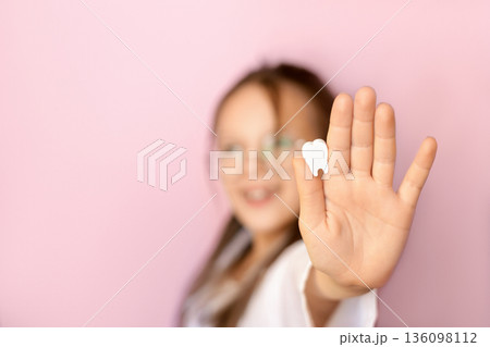 Kid showing tooth icon in hand on pink background. Concept of World Oral Health Day, dental care, oral hygiene, children health awareness and prevention. 136098112