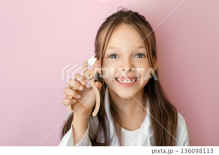 Smiling child holding a lost baby tooth on pink background. World Oral Health Day concept focused on pediatric dentistry, oral hygiene, prevention and healthy childhood development. 136098113