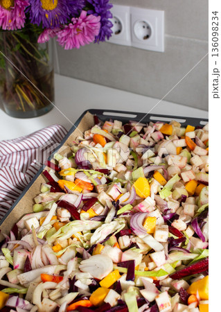Fresh vegetables are chopped and placed on a baking tray ready for cooking in the oven. Colorful ingredients are showcased, and the setting is a welcoming kitchen 136098234