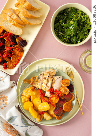 Baked potato is served with chicken breast and roasted carrots, peppers, and beets on a plate. A light meal is arranged on a simple table setting Baked potato is served with chicken breast and roasted carrots, peppers, and beets on a plate. A light meal is arranged on a simple table setting 136098236