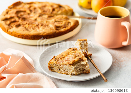 A slice of pear pie sits on a white plate with a fork. A warm coffee cup is next to it. Fresh pears are placed on the table, adding to the scene A slice of pear pie sits on a white plate with a fork. A warm coffee cup is next to it. Fresh pears are placed on the table, adding to the scene 136098618